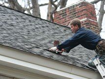 Roofer hammering shingles on a brown-shingle roof